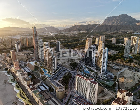 bright sunset over elegant waterfront towers, golden hour illuminates upscale skyscrapers near mountains 135720110