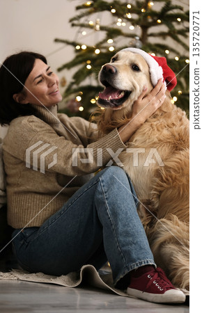 Woman Wearing A Santa Hat With Golden Retriever Dog At Home During Christmas Time Woman Wearing A Santa Hat With Golden Retriever Dog At Home During Christmas Time 135720771