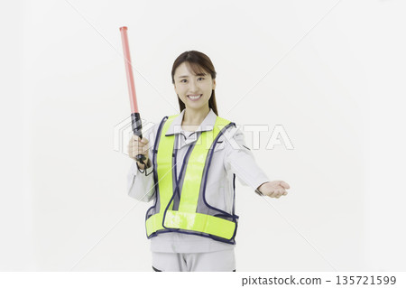一位年輕的日本女性身穿工作服，繫著安全帶，手持緊急出口標誌，背景為白色。 135721599