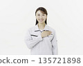 A young Japanese woman in work clothes holding her hand on her chest against a white background 135721898
