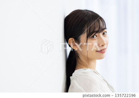 一位微笑的年輕女子倚靠在白牆上。 135722196