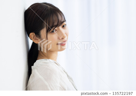 一位微笑的年輕女子倚靠在白牆上。 135722197