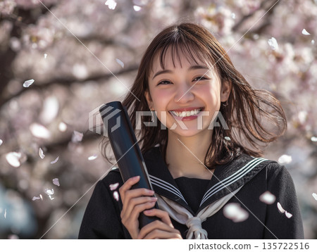 A high school girl smiling with a diploma in hand under cherry blossoms in full bloom on graduation day 135722516