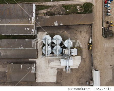 Drone overhead of grain storage plant with round metal silos and conveyor lines beside farm warehouses and service yard Drone overhead of grain storage plant with round metal silos and conveyor lines beside farm warehouses and service yard 135723812