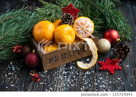 Orange mandarins in wooden box with fir apple, red balls, snowflakes on green fir branch background. Christmas card. Happy new year and merry christmas. High quality photo Orange mandarins in wooden box with fir apple, red balls, snowflakes on green fir branch background. Christmas card. Happy new year and merry christmas. High quality photo 135724941