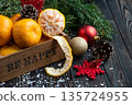 Orange mandarins in wooden box with fir apple, red balls, snowflakes on green fir branch background. Christmas card. Happy new year and merry christmas. High quality photo 135724955