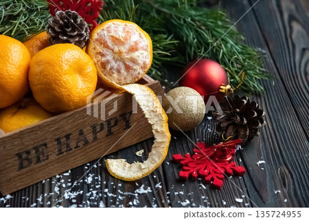 Orange mandarins in wooden box with fir apple, red balls, snowflakes on green fir branch background. Christmas card. Happy new year and merry christmas. High quality photo Orange mandarins in wooden box with fir apple, red balls, snowflakes on green fir branch background. Christmas card. Happy new year and merry christmas. High quality photo 135724955