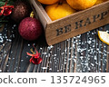 Orange mandarins in wooden box with fir apple, red balls, snowflakes on green fir branch background. Christmas card. Happy new year and merry christmas. High quality photo 135724965