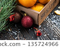 Orange mandarins in wooden box with fir apple, red balls, snowflakes on green fir branch background. Christmas card. Happy new year and merry christmas. High quality photo 135724966