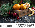 Orange mandarins in wooden box with fir apple, red balls, snowflakes on green fir branch background. Christmas card. Happy new year and merry christmas. High quality photo 135724967
