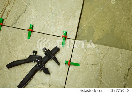 A professional tiler is carefully positioning a ceramic wall tile onto a layer of fresh adhesive, utilizing a lash tile leveling system for a perfectly flat surface. A professional tiler is carefully positioning a ceramic wall tile onto a layer of fresh adhesive, utilizing a lash tile leveling system for a perfectly flat surface. 135725020