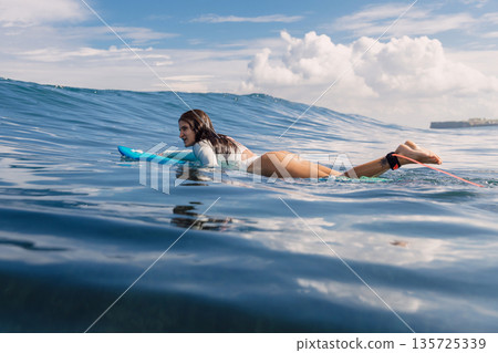 Surfgirl floating on surfboard. Attractive surfer woman in ocean during surfing Surfgirl floating on surfboard. Attractive surfer woman in ocean during surfing 135725339
