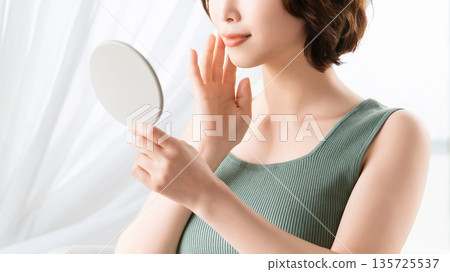 Woman checking her skin in the mirror - beauty image 135725537