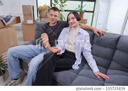 Couple enjoys a cozy moment on a sofa surrounded by moving boxes in their new home 135725839