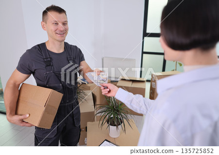 Delivery person hands over cash as payment in a modern office space filled with boxes 135725852