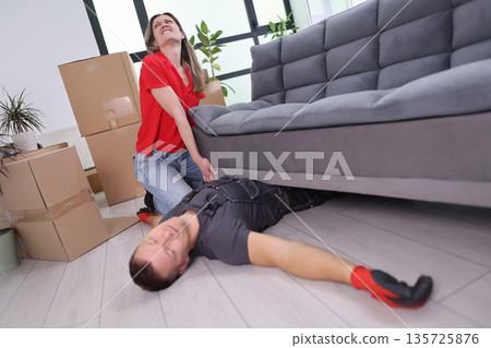 Moving day chaos as laughter and mishaps unfold while lifting a heavy couch with friends in a bright living room 135725876