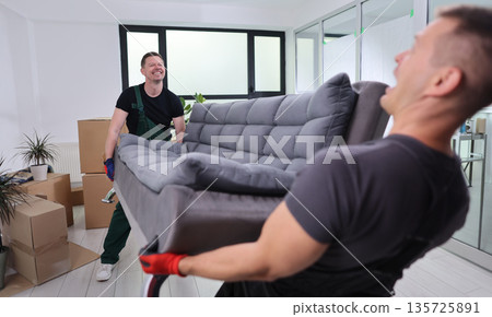 Movers joyfully lifting a cozy gray sofa during a bright, sunny afternoon in a modern living room Movers joyfully lifting a cozy gray sofa during a bright, sunny afternoon in a modern living room 135725891