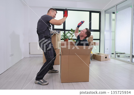 Two friends joyfully playing in cardboard boxes while moving into a new apartment during a sunny afternoon Two friends joyfully playing in cardboard boxes while moving into a new apartment during a sunny afternoon 135725934