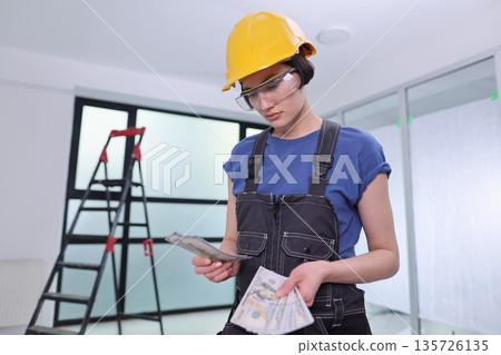 Young construction worker counting cash and planning the next steps in a modern office renovation at midday 135726135