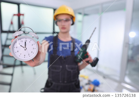 Skilled worker showcases urgency in construction with clock and power tool in modern workspace 135726138
