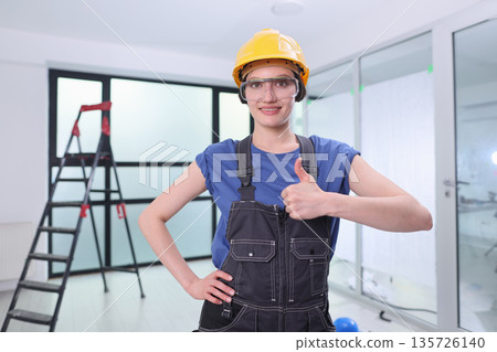 Busy construction site where a woman stands proudly in a hard hat and overalls, ready to tackle tasks with a smile and enthusiasm 135726140