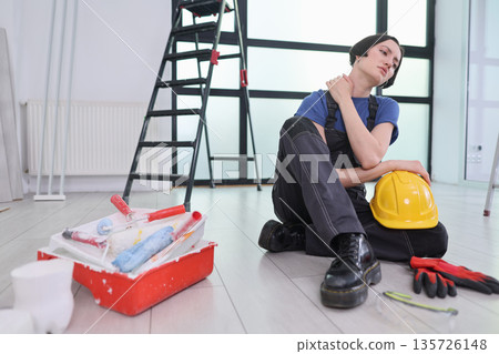 Hardworking painter takes a break on the floor in a bright room surrounded by tools and equipment Hardworking painter takes a break on the floor in a bright room surrounded by tools and equipment 135726148