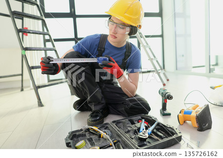 Young worker inspects tools while preparing for a construction task in a bright, spacious indoor setting 135726162
