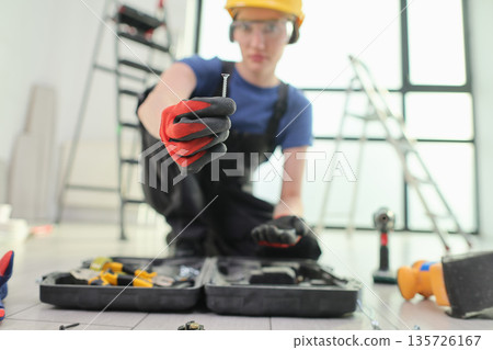 Skilled worker demonstrates precision with a screw while organizing tools in a bright workshop space Skilled worker demonstrates precision with a screw while organizing tools in a bright workshop space 135726167