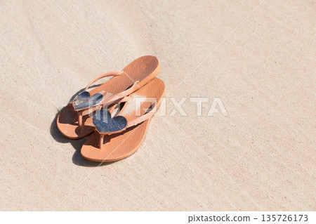 A pair of tan flip flops with shiny heart decorations A pair of tan flip flops with shiny heart decorations 135726173