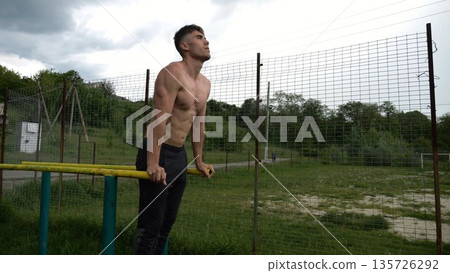 Young sportsman doing push ups on parallel bars at nature. Strong sporty man exercising at sports ground. Male shirtless athlete training hard outdoor. Concept of active sportive lifestyle. Slow mo 135726292
