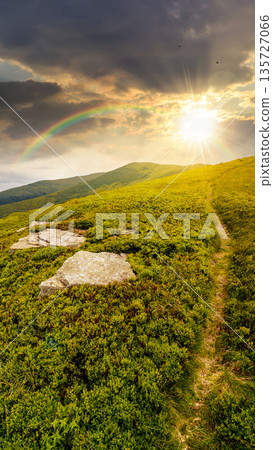 hiking trail through mountain landscape at sunset. mountain range under sky with clouds in evening light. scenery with green grass and rolling hills. timeless nostalgia book cover with rainbow hiking trail through mountain landscape at sunset. mountain range under sky with clouds in evening light. scenery with green grass and rolling hills. timeless nostalgia book cover with rainbow 135727066