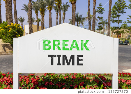 Break time symbol. Concept word Break time on beautiful white billboard. Beautiful blue sky and palm tree flowers background. Business break time concept. Copy space. Break time symbol. Concept word Break time on beautiful white billboard. Beautiful blue sky and palm tree flowers background. Business break time concept. Copy space. 135727270