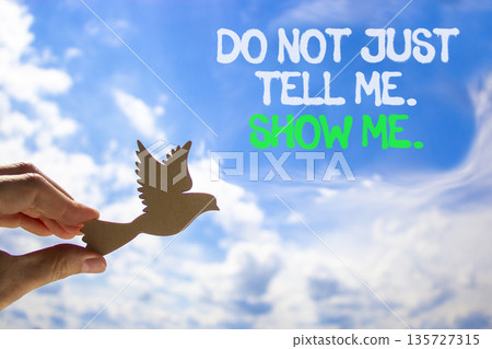 Tell or show symbol. Concept words Do not just tell me, show me on beautiful blue sky. Beautiful blue sky background. Businessman's hand with wooden bird. Business tell or show concept. Copy space. 135727315
