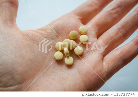 Human hand holding multiple yellow tablets 135727774