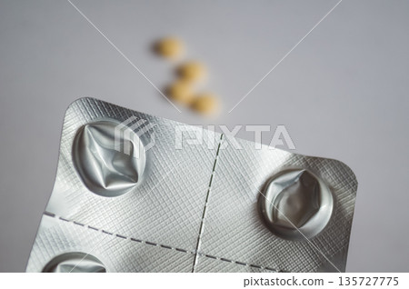 Used aluminum blister pack with yellow pills in the background 135727775