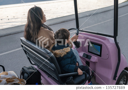 Mother And Child Enjoying A Ride In A Charming Electric Cart By Water. Mother And Child Enjoying A Ride In A Charming Electric Cart By Water. 135727889