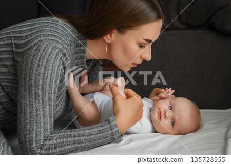 A young mother bent at the little baby, at home. 135728955