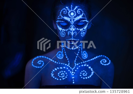 Body art on the body and hand of a girl glowing in the ultraviolet light. 135728961