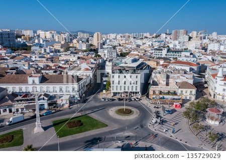 Visitors walk through the streets of Faro's Old Town near the dock area, enjoying the architecture and local shops under clear blue skies in Algarve 135729029