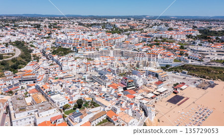 People relax at Praia dos Pescadores while families walk along the beach. The marina is busy with boats and the town of Albufeira is vibrant 135729053