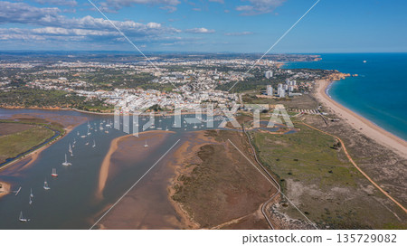 Scenic aerial view of coastal landscape featuring boats, sandy beaches, and vibrant greenery, showcasing the beauty of a popular tourist destination. Alvor Portugal Algarve Scenic aerial view of coastal landscape featuring boats, sandy beaches, and vibrant greenery, showcasing the beauty of a popular tourist destination. Alvor Portugal Algarve 135729082