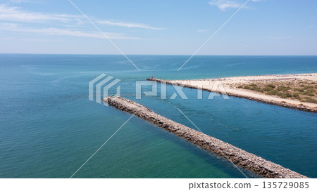 Serene coastal view featuring a stone jetty extending into calm turquoise waters, ideal for relaxation and beach activities. Tavira Portugal Algarve 135729085