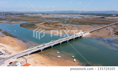 This aerial view captures the beauty of Ria Formosa and Praia de Faro in Portugal. The image shows the new bridge, boats, and waterways in the region This aerial view captures the beauty of Ria Formosa and Praia de Faro in Portugal. The image shows the new bridge, boats, and waterways in the region 135729105