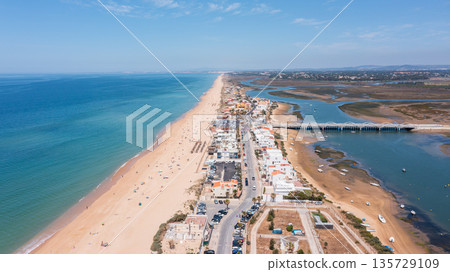 Aerial view shows Praia de Faro with its long sandy beach and the nearby Ria Formosa. People enjoy the beach while boats rest in the water 135729109