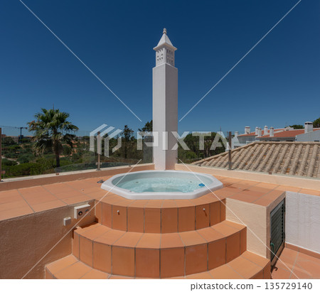 A hot tub sits on a rooftop terrace with steps leading up to it. Surrounding palm trees can be seen under a clear blue sky in a sunny weather A hot tub sits on a rooftop terrace with steps leading up to it. Surrounding palm trees can be seen under a clear blue sky in a sunny weather 135729140