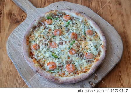 Delicious pizza supreme topped with shrimp, green peppers, and cheese, served on a wooden board, showcasing vibrant colors and appetizing textures Delicious pizza supreme topped with shrimp, green peppers, and cheese, served on a wooden board, showcasing vibrant colors and appetizing textures 135729147