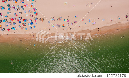 Aerial view of vibrant beach scene with colorful umbrellas and sunbathers enjoying sunny day by the ocean, capturing summer leisure atmosphere. Tavira Portugal Algarve Aerial view of vibrant beach scene with colorful umbrellas and sunbathers enjoying sunny day by the ocean, capturing summer leisure atmosphere. Tavira Portugal Algarve 135729178