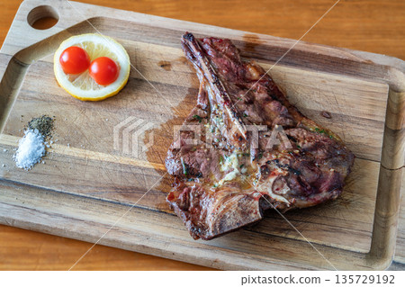 T-bone steak grilled to perfection on a wooden cutting board, garnished with lemon and cherry tomatoes, showcasing delicious culinary presentation T-bone steak grilled to perfection on a wooden cutting board, garnished with lemon and cherry tomatoes, showcasing delicious culinary presentation 135729192