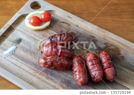 Grilled sausages on a wooden cutting board with fresh tomatoes and lemon, showcasing vibrant colors and textures for culinary inspiration Grilled sausages on a wooden cutting board with fresh tomatoes and lemon, showcasing vibrant colors and textures for culinary inspiration 135729194
