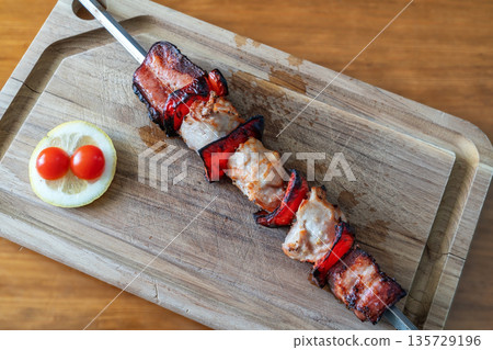 Grilled chicken and bacon skewers on a wooden cutting board, garnished with cherry tomatoes and lemon, perfect for outdoor barbecues and gatherings Grilled chicken and bacon skewers on a wooden cutting board, garnished with cherry tomatoes and lemon, perfect for outdoor barbecues and gatherings 135729196